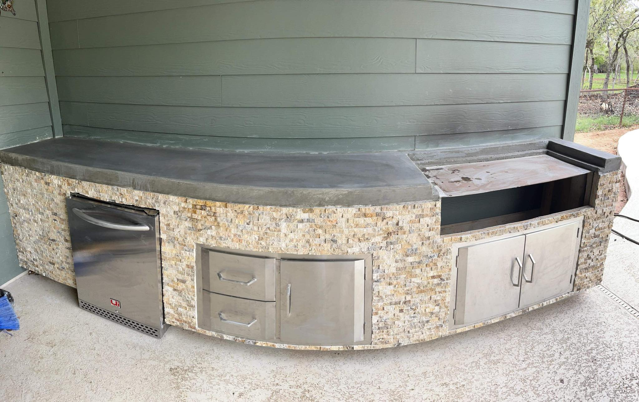 Custom outdoor kitchen with concrete countertops, stone veneer, stainless steel storage, and built-in grill area in Granbury, TX.