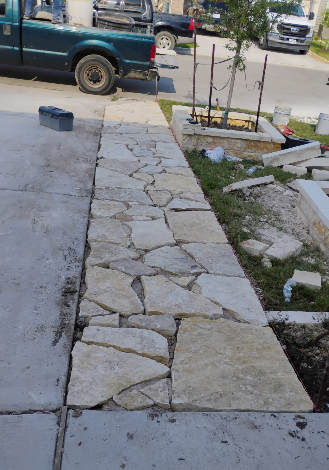 Custom flagstone sidewalk installation connecting a concrete driveway to decorative landscape planters at a residential property in Central Texas.