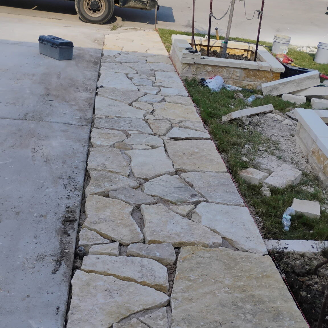 custom-flagstone-sidewalk-installation-central-texas.jpg Custom flagstone sidewalk installation connecting a concrete driveway to decorative landscape planters at a residential property in Central Texas.