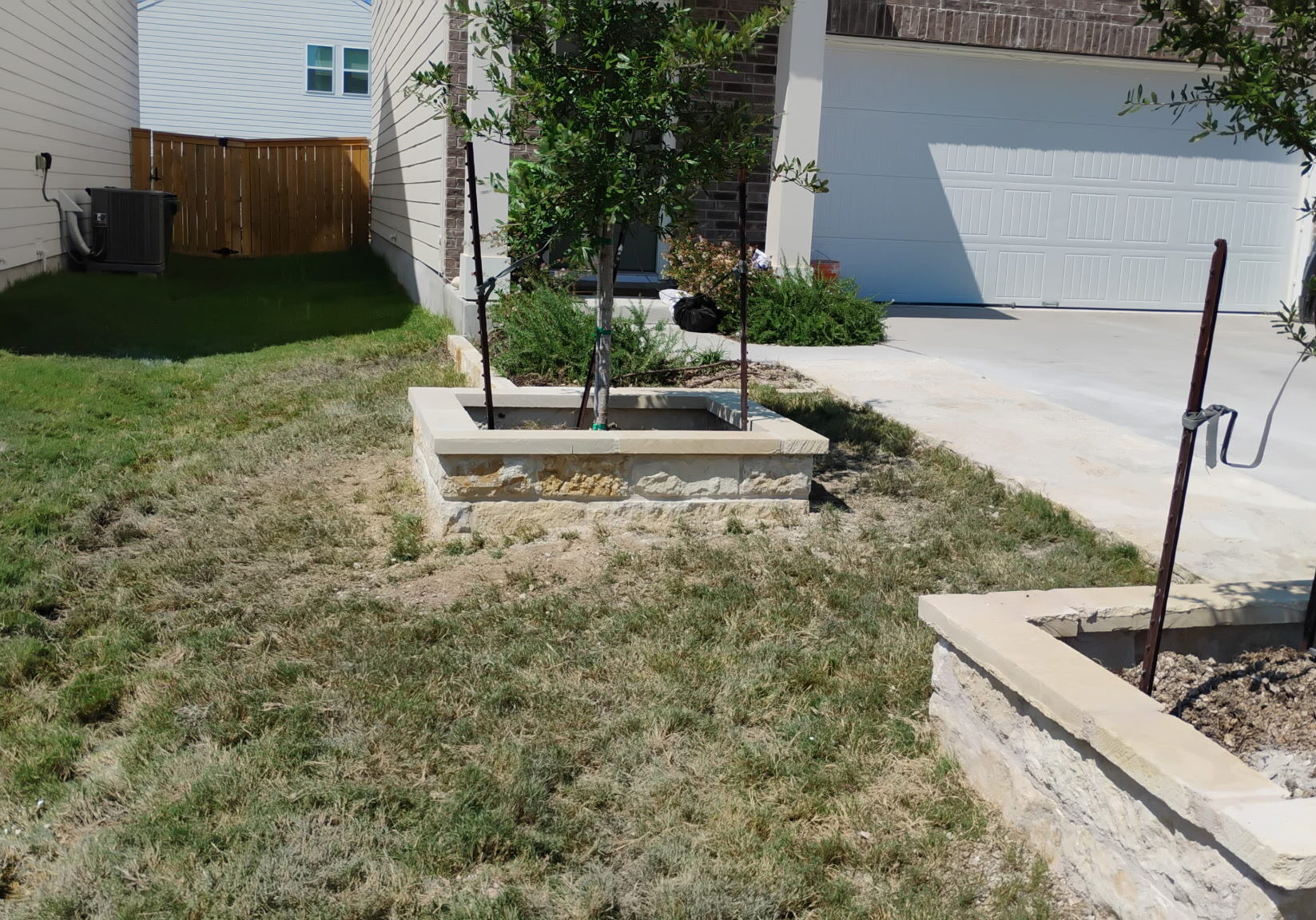 Custom concrete and stone tree planters installed along a residential driveway to enhance curb appeal and landscaping in Central Texas.