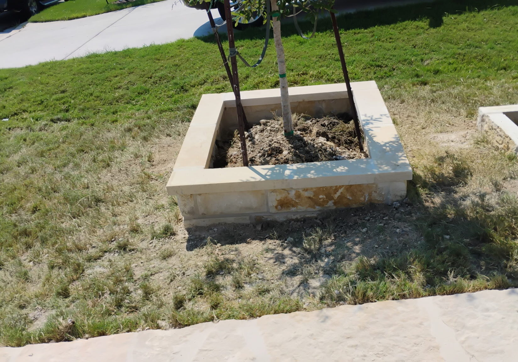 Custom stone tree planter built with natural limestone and decorative capstone as part of a residential landscape enhancement project in Central Texas.