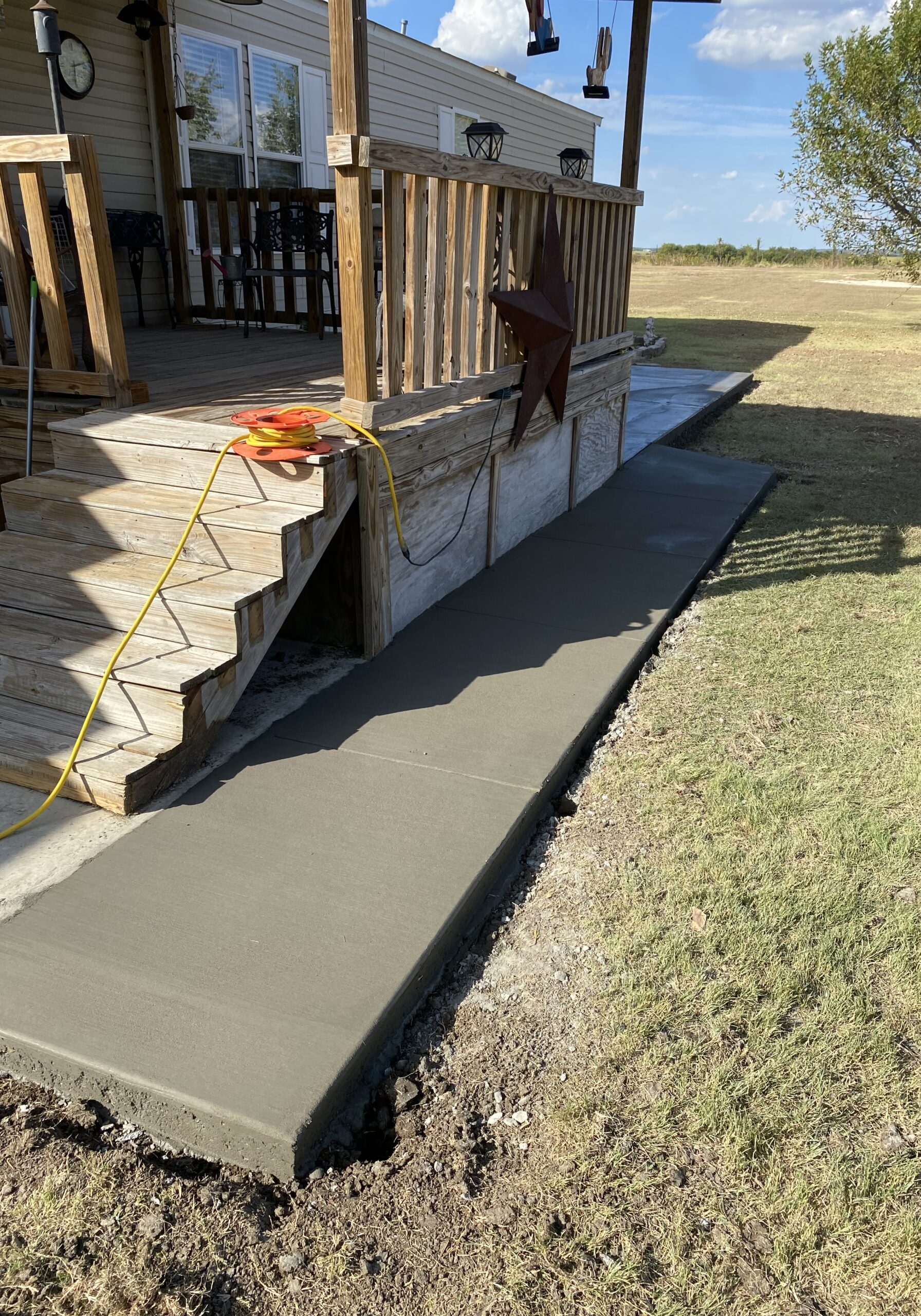 New concrete walkway installation connecting a covered porch to a backyard patio area at a residential property in Central Texas.