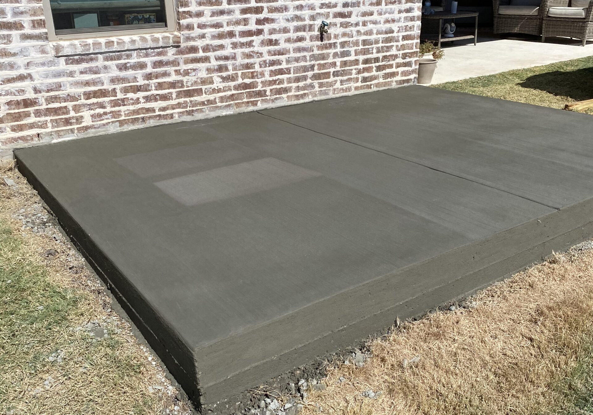 New residential concrete patio installation completed behind a brick home, providing a durable outdoor living space in Central Texas.